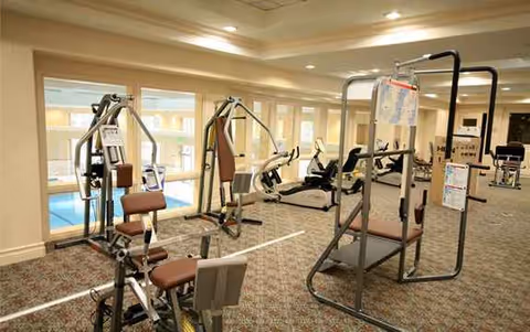 Indoor fitness room with various exercise machines and carpeted floor at La Costa Glen.