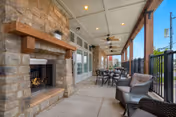 Covered outdoor patio with a stone fireplace, wicker seating, dining tables, and ceiling fans overlooking the street.