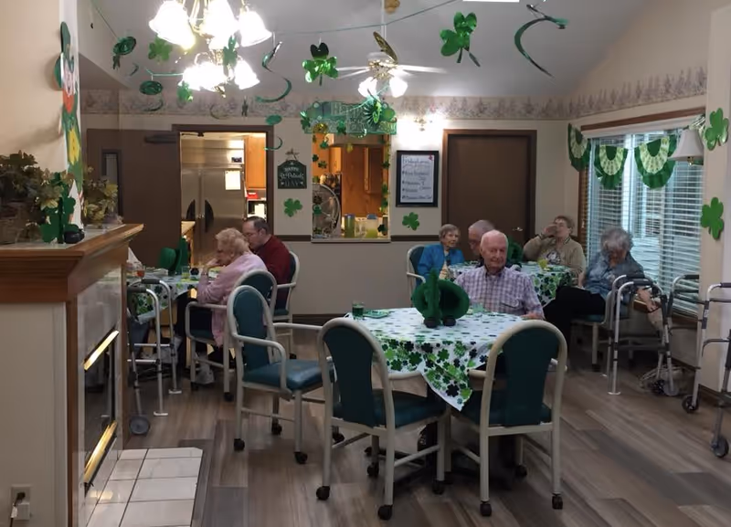 Residents sitting at tables in a shamrock-decorated dining room of a senior living facility.