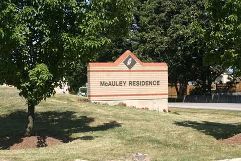 Outdoor sign reading McAULEY RESIDENCE with trees and grass around.