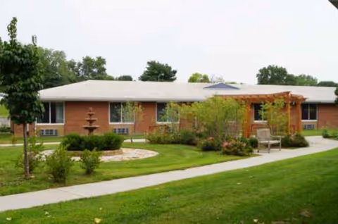 Exterior view of a single-story brick senior living facility with a landscaped courtyard and pathway.
