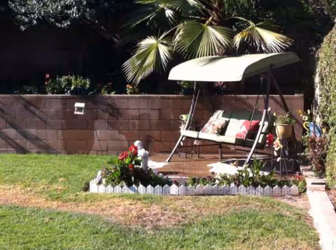 Outdoor garden area with a shaded swing bench and small planted flower bed.