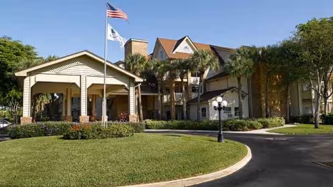 Meridian at Lantana senior living facility exterior with entrance, flags, and palm trees.