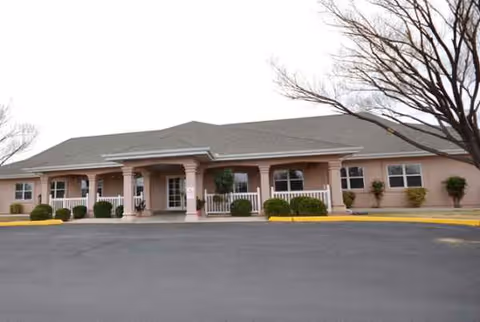 Single-story pink senior living facility front entrance with columns and trimmed shrubs