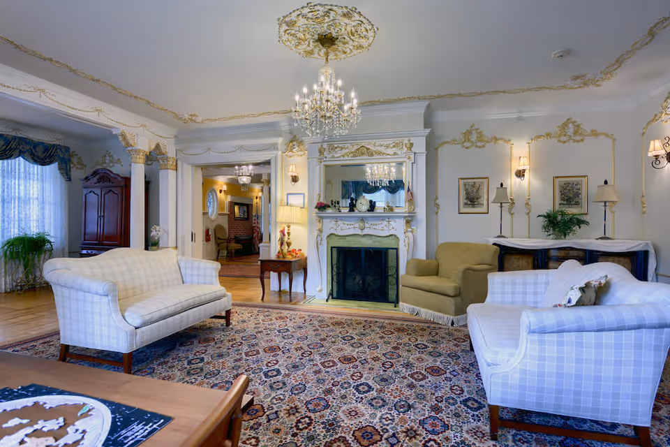 Elegant traditional living room with upholstered sofas, a patterned area rug, ornate fireplace and mirror, and a crystal chandelier.