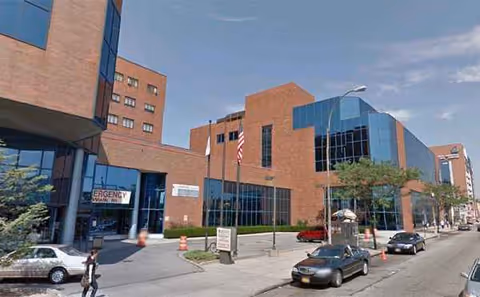 Exterior view of Jamaica Hospital Medical Center building with blue glass facade and flags.
