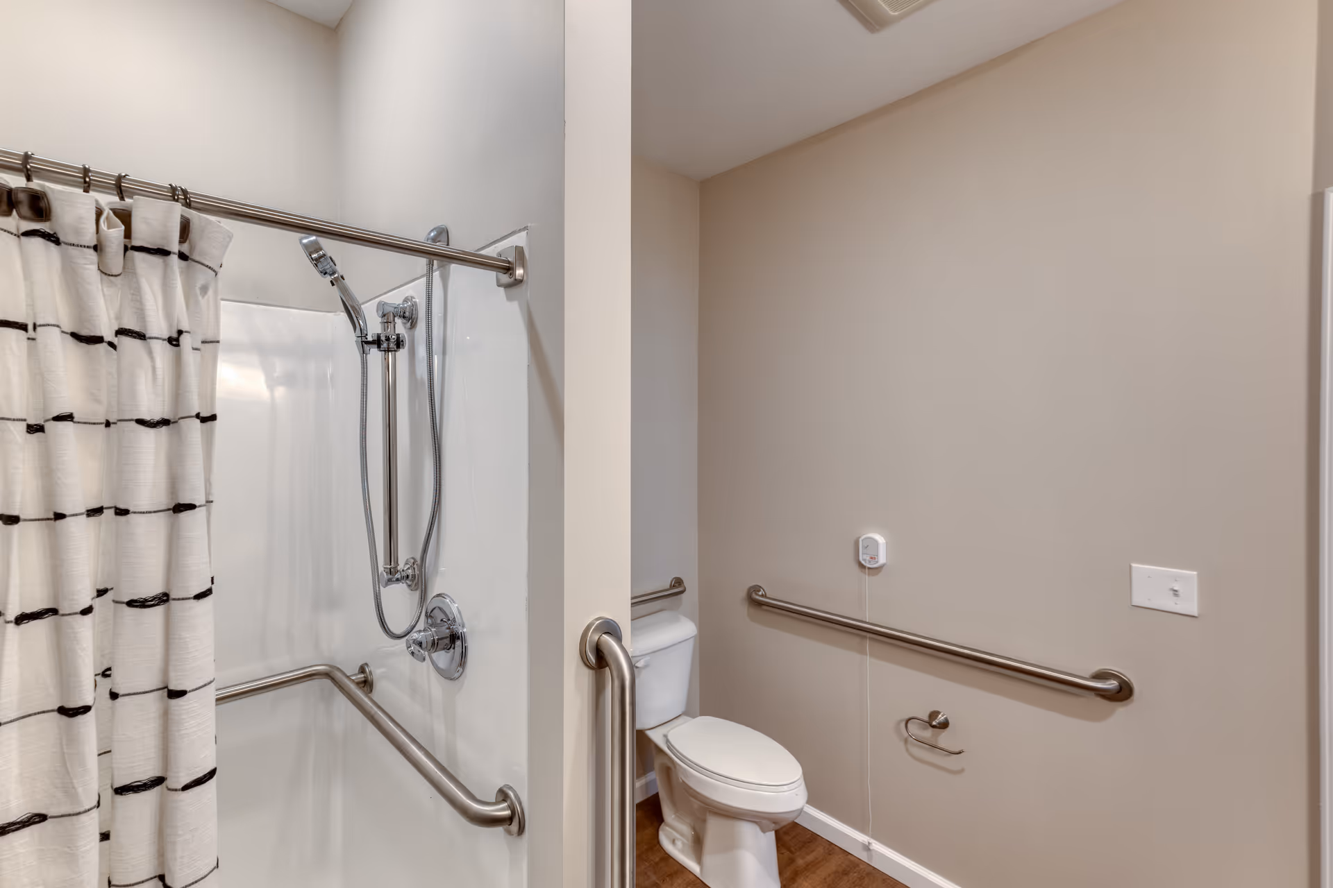 Accessible bathroom with a shower and toilet, featuring stainless grab bars and a striped shower curtain.