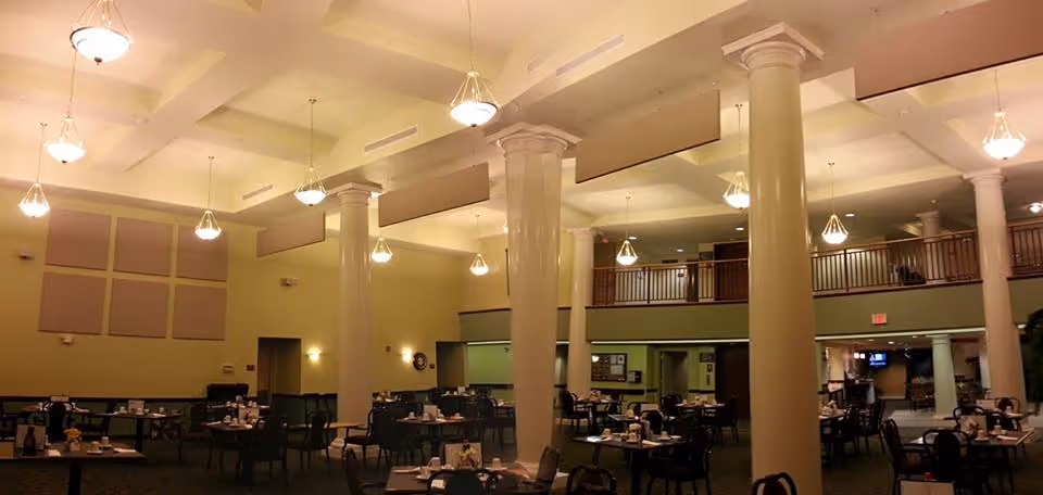Large dining room with multiple tables and chairs beneath high ceilings and tall columns.