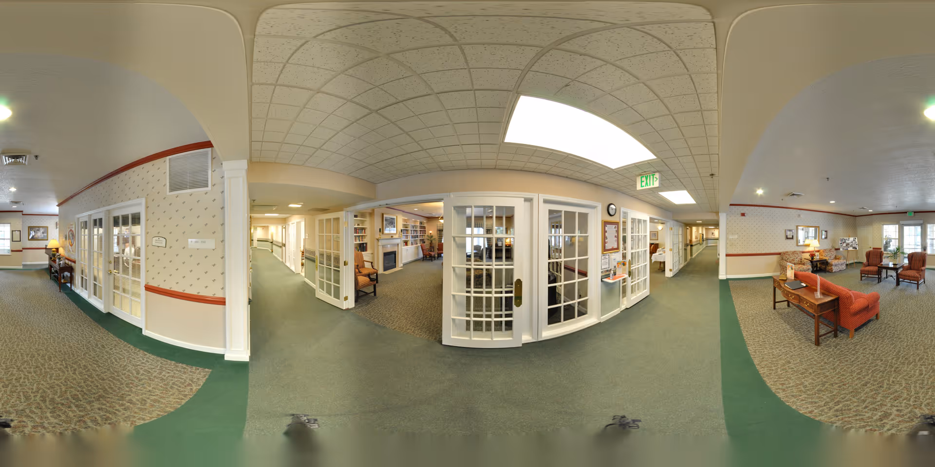 Panoramic view of Oak Woods Manor's interior common area with seating, French doors opening to a fireplace and bookshelf room, and hallways on either side.