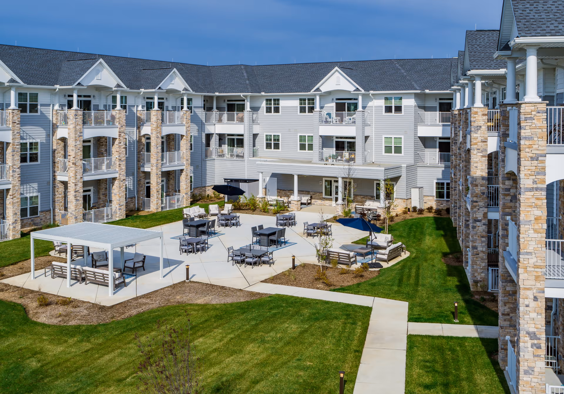 Outdoor courtyard of a multi-story senior living building with patio seating, umbrellas, and green lawn.