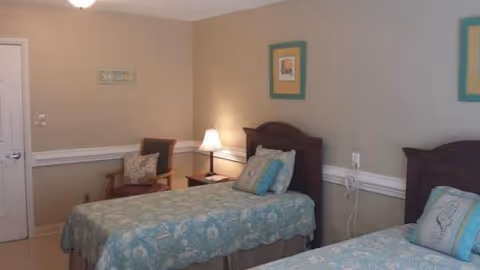 Two twin beds with matching headboards and pastel bedding in a beige memory care room.