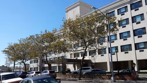 Exterior view of a multi-story senior living building with cars and trees.