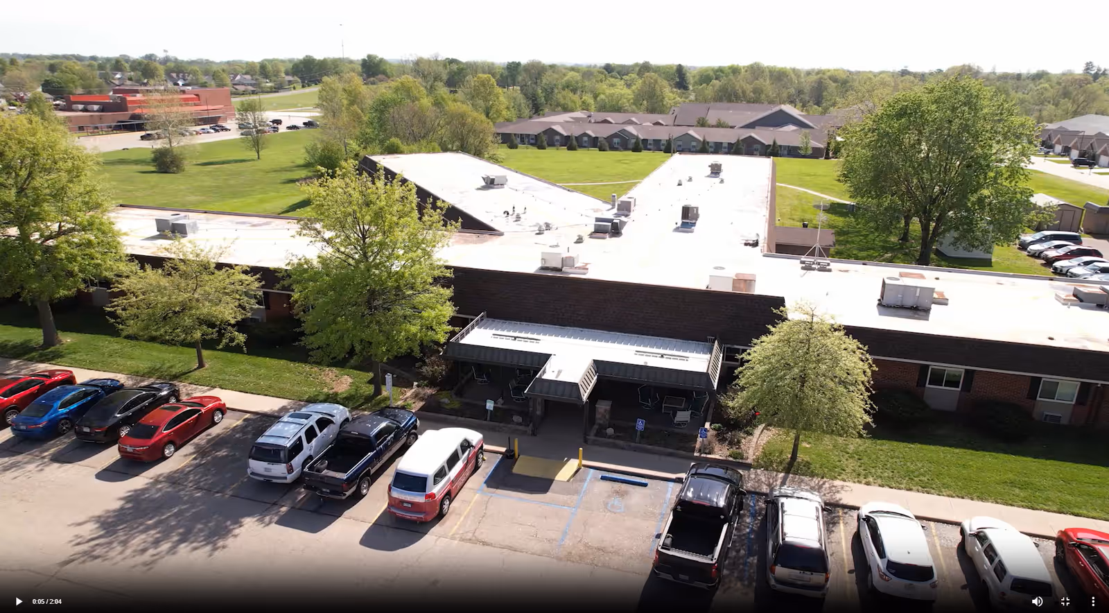 Aerial view of Jackson Manor's single-story building entrance with parked cars, trees, and surrounding lawns.