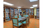 A cozy library room with bookshelves along the walls and a table surrounded by chairs in the center.