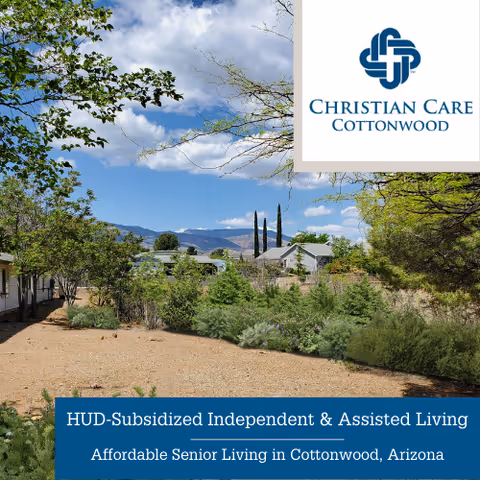 Landscaped courtyard with shrubs and trees, single-story buildings and distant mountains under a blue sky.