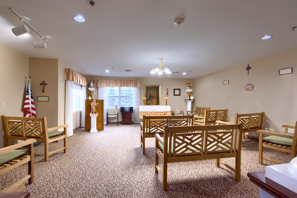 Carpeted interior common room with wooden chairs arranged facing a small altar and religious decorations.