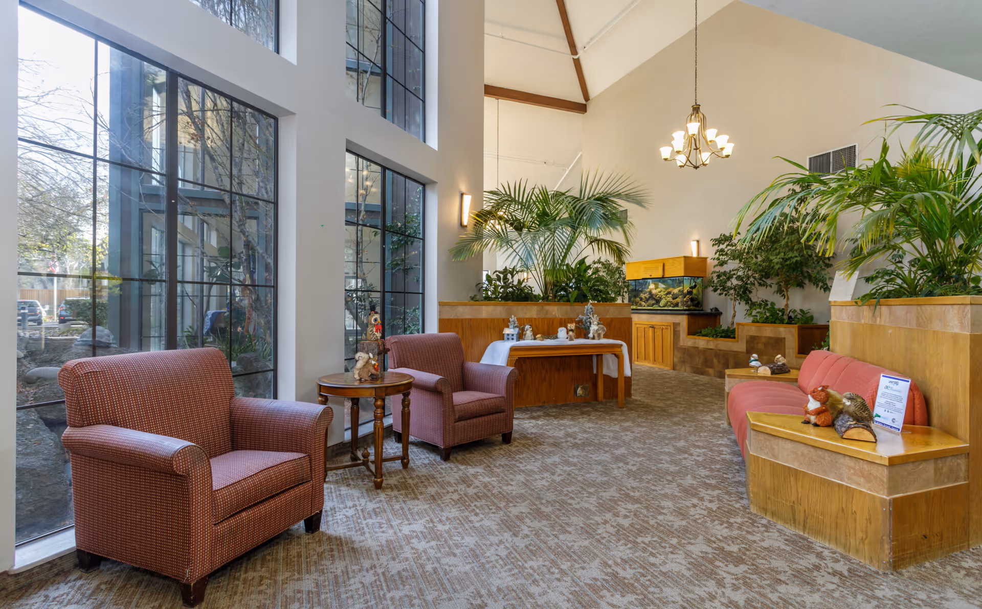 Bright lobby seating area with armchairs, large windows, indoor plants, and an aquarium.