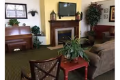 Cozy common room with a fireplace and wall-mounted TV, seating, a piano, and potted plants.
