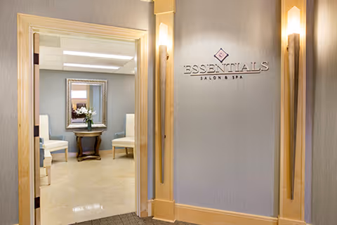 Entrance to the Essentials Salon & Spa with wall signage and a doorway leading to a small seating area with chairs and a mirror.