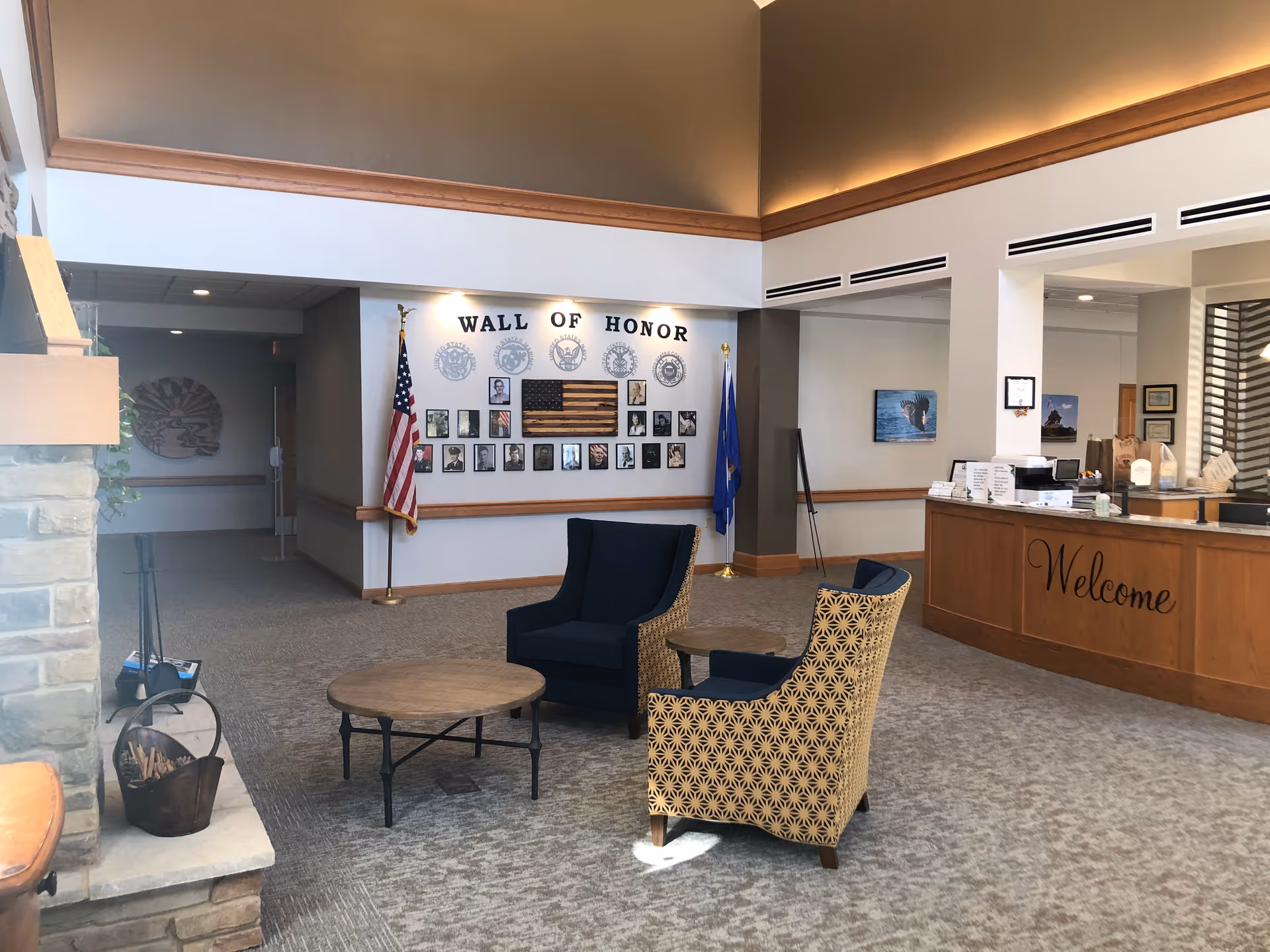 Reception lobby with chairs and tables, a 'Wall of Honor' display with flags, and a welcome desk.