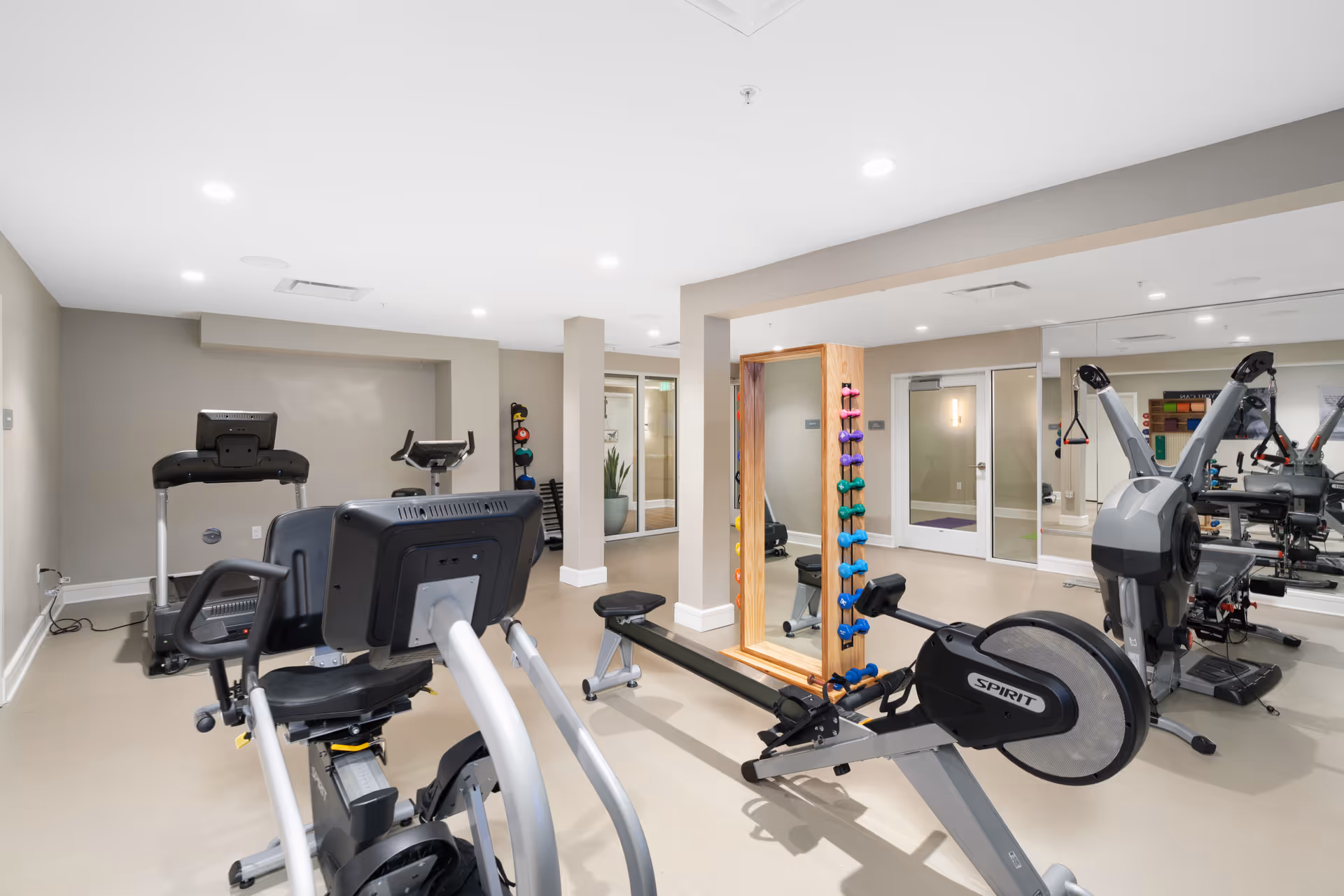 Bright fitness room with exercise equipment, dumbbells, mirrors and a rowing machine.