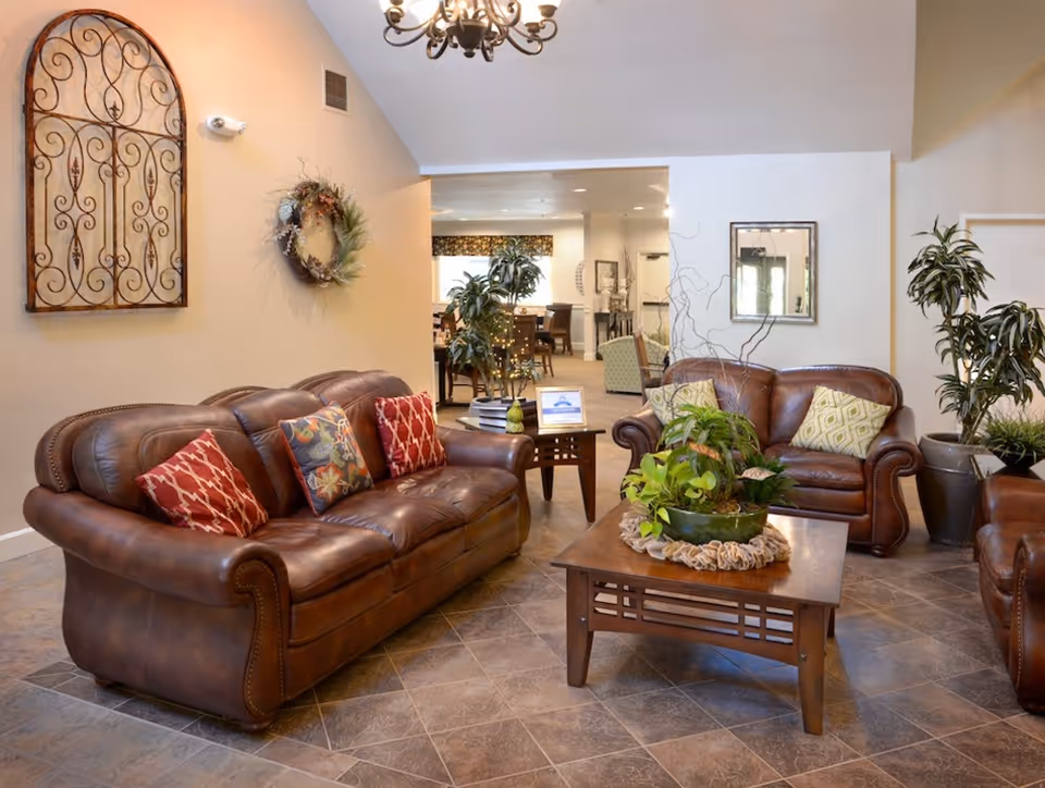 Cozy common living room with brown leather sofas, a wooden coffee table topped with plants, and decorative wall accents.