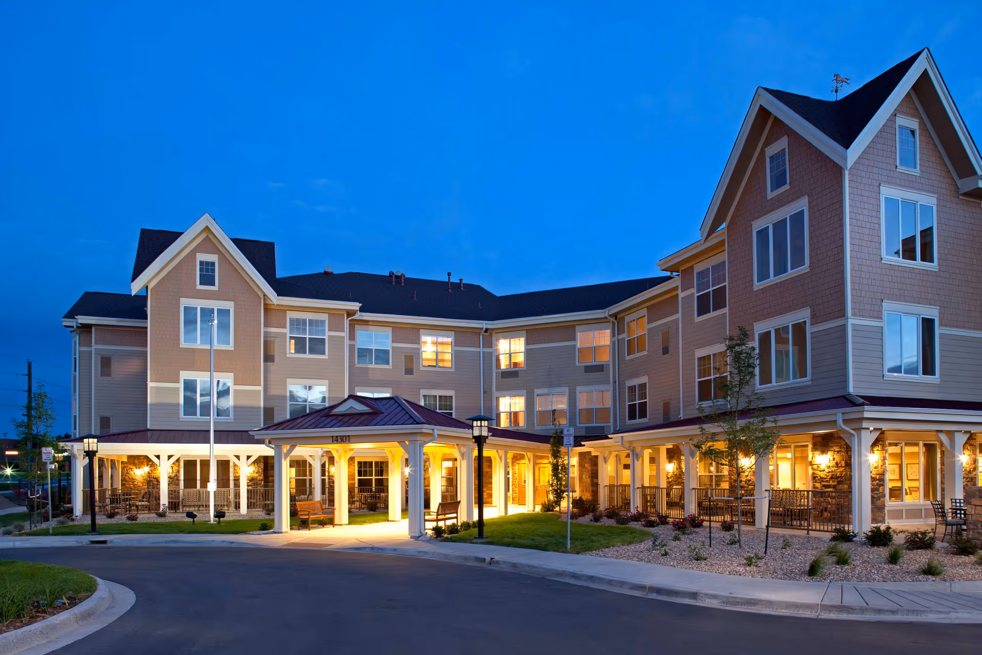 Exterior view of MorningStar Assisted Living & Memory Care at Jordan building at dusk, showing a well-lit entrance with a covered drop-off area, multiple windows, and landscaped surroundings.