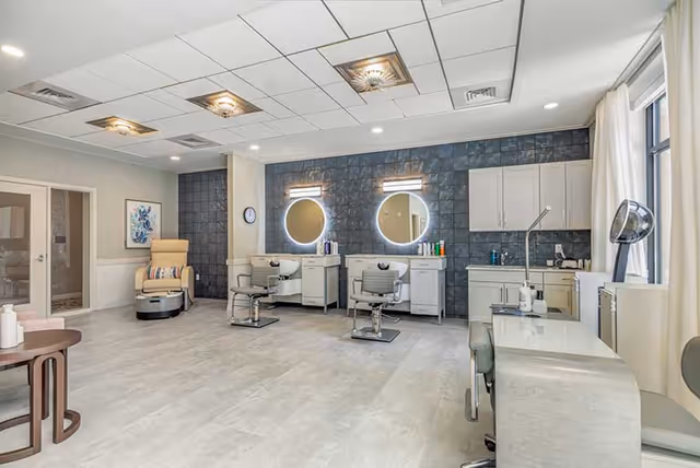 Bright salon-style grooming room with styling chairs, illuminated round mirrors, manicure stations, and a pedicure chair.