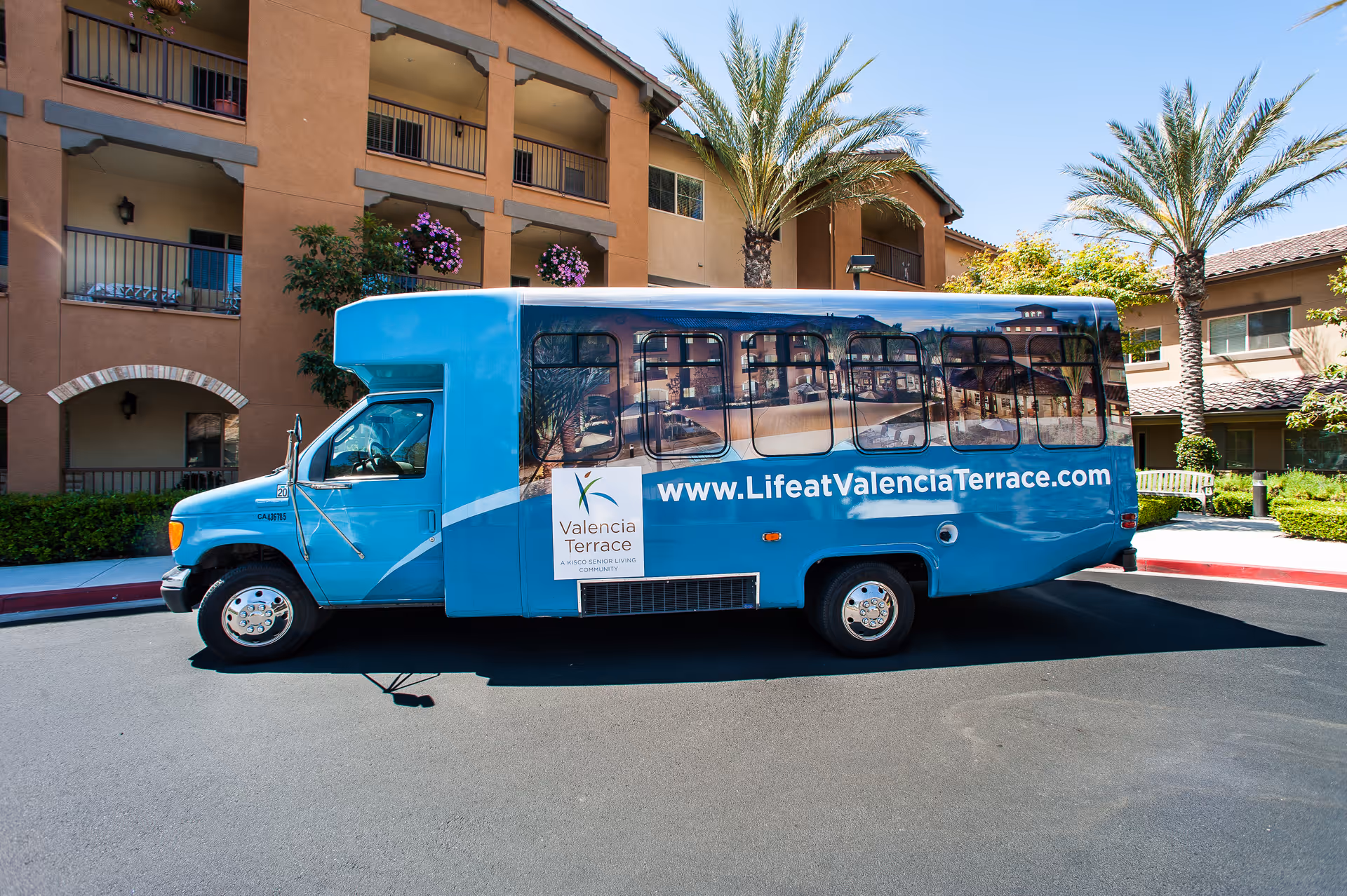 A blue Valencia Terrace shuttle bus parked in front of a senior living building with palm trees.