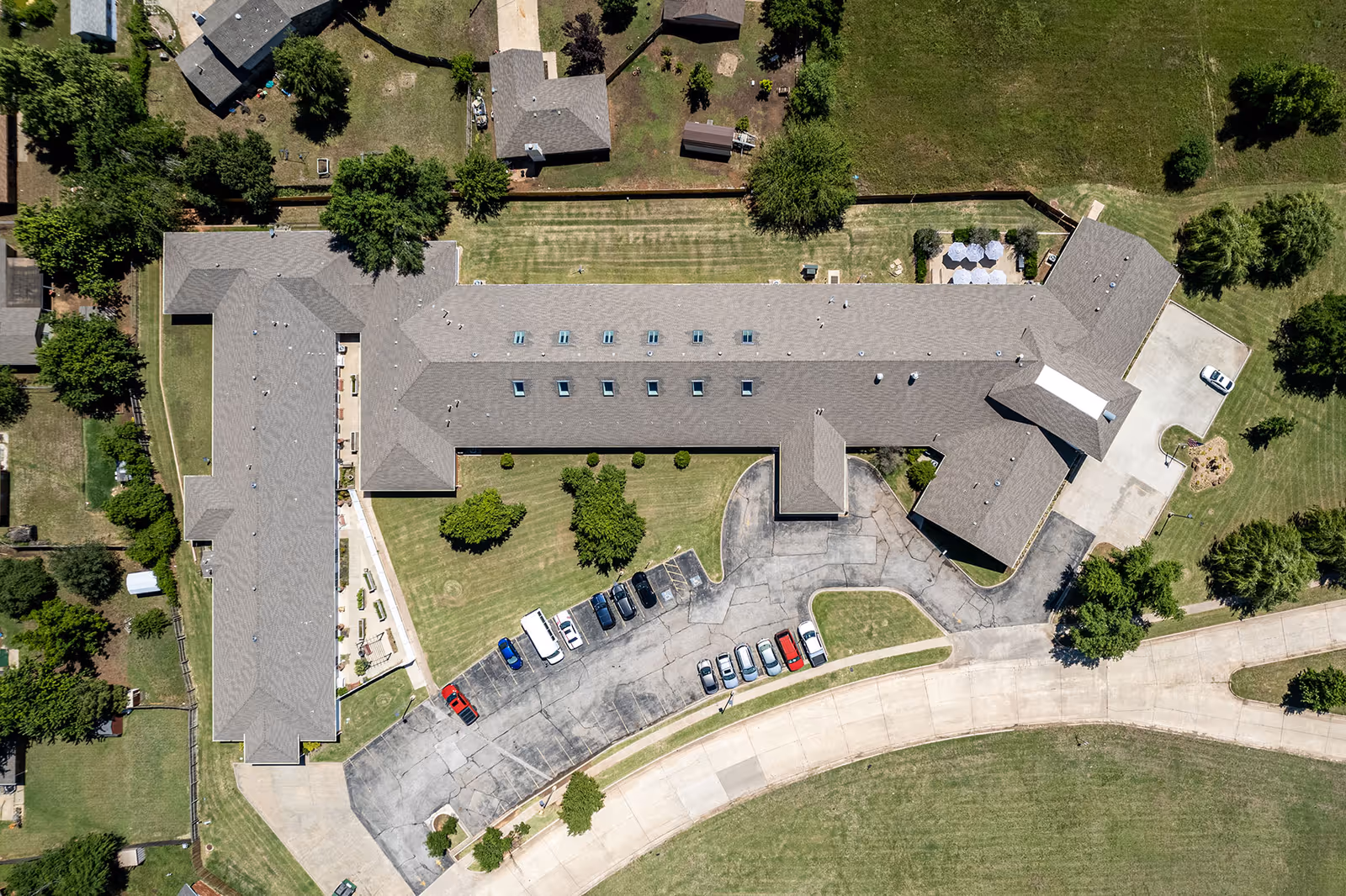 Aerial top-down view of a senior living facility building with adjacent parking lot, driveways, and surrounding lawns.