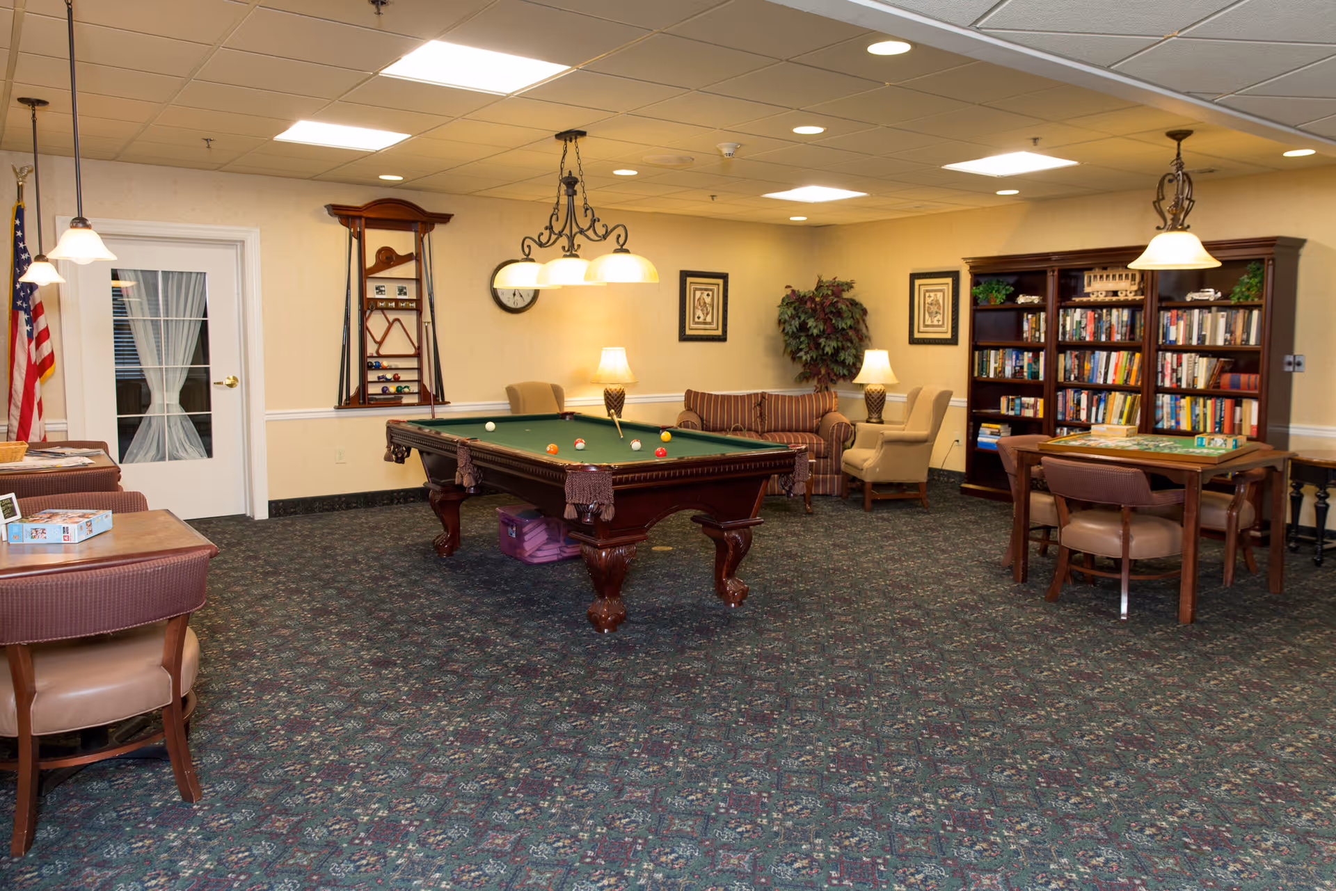 A communal lounge with a pool table, seating areas, bookshelves, and overhead lighting.