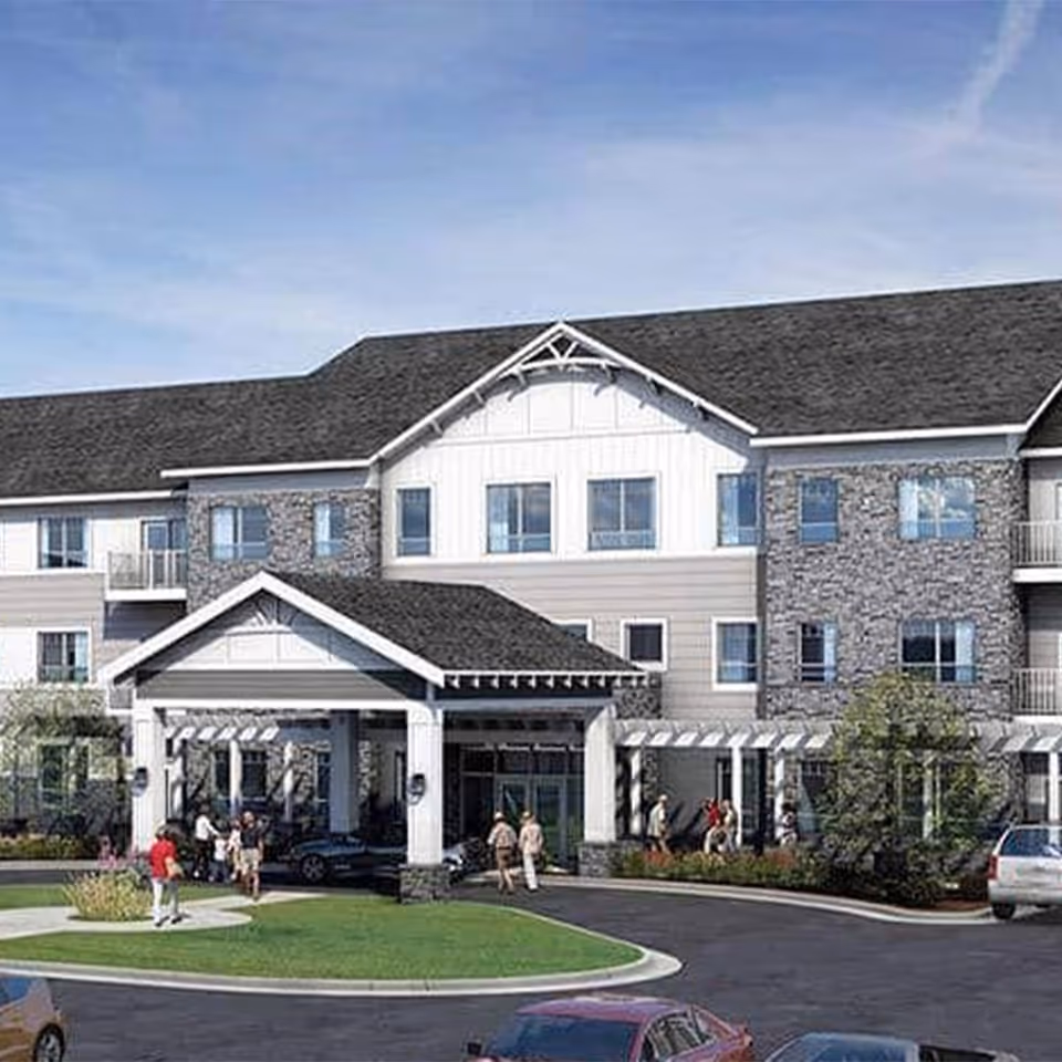 Front exterior of a three-story senior living building with a covered entrance, circular drive, and people near the entrance.