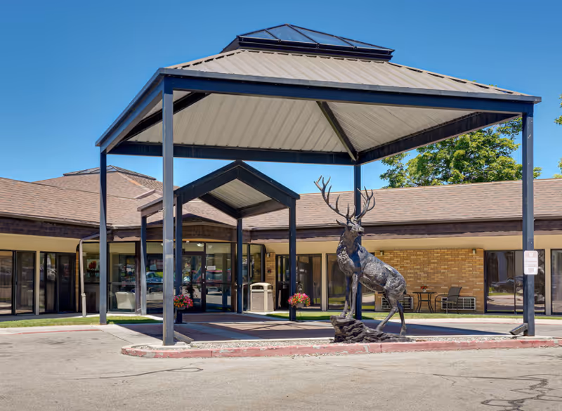 Covered main entrance of a single-story building with a large metal canopy and a stag sculpture in front.