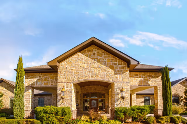 Stone-faced building facade with a central arched entrance and manicured landscaping.
