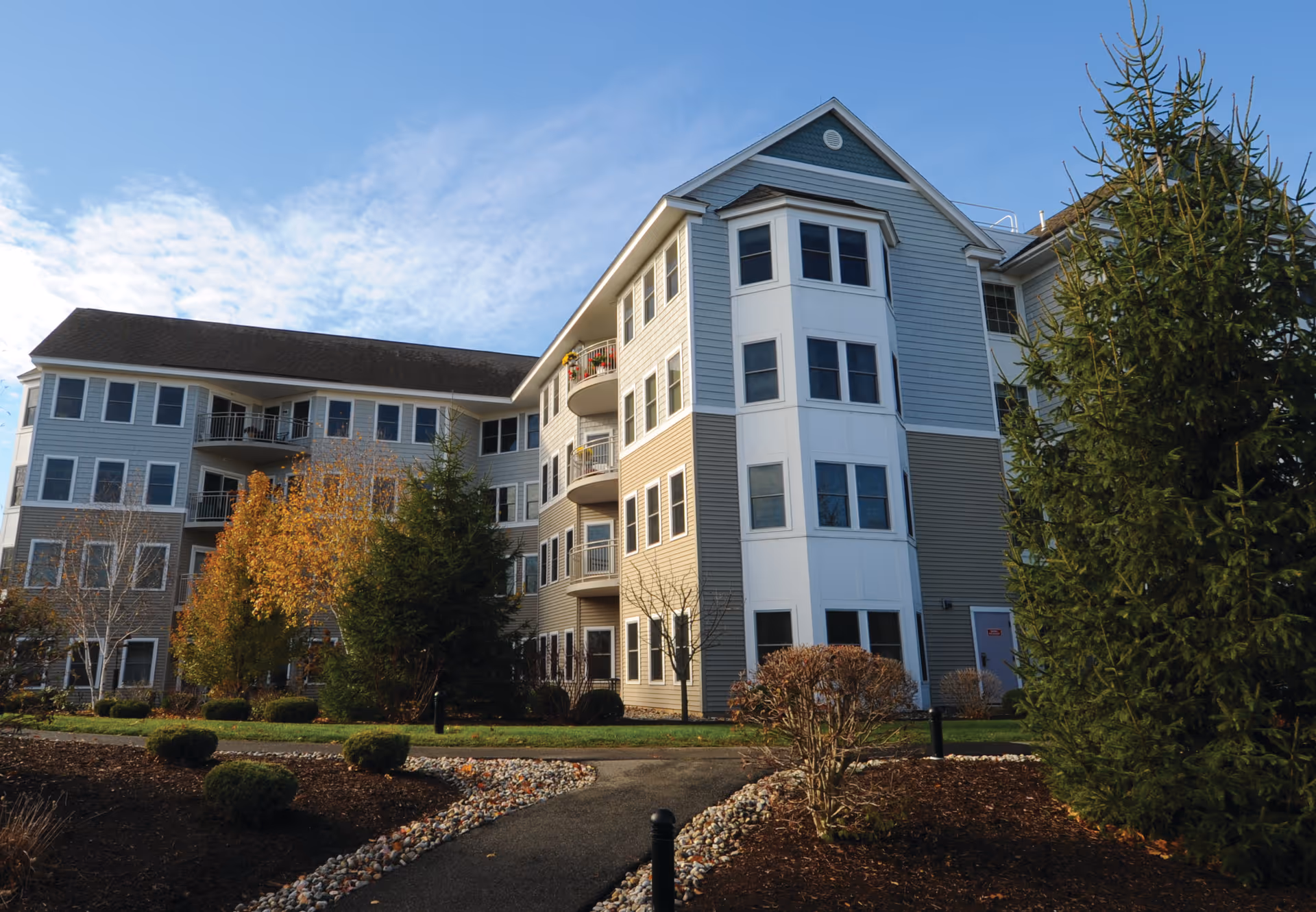 Multi-story senior living building with balconies and landscaped grounds under a blue sky.
