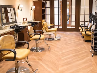 Interior salon area with multiple yellow styling chairs, shampoo sinks, mirrors, and wood cabinets.