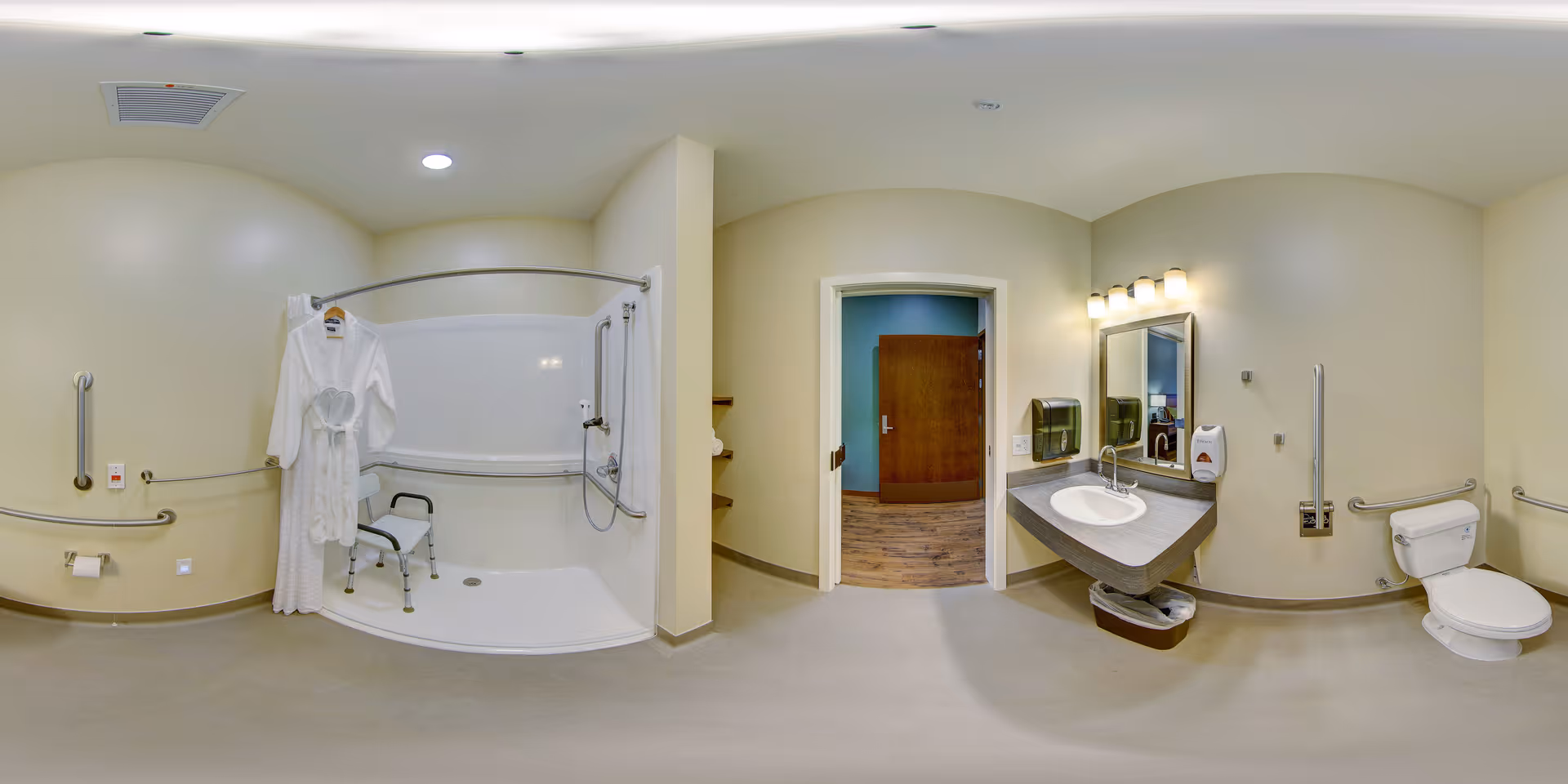 Accessible senior bathroom with a roll-in shower and shower chair, multiple grab bars, a sink and mirror with soap dispenser, and a toilet with grab rails, seen with an open doorway to a hallway.
