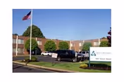 Exterior view of Silver Lake Healthcare Center building with a flagpole flying the American flag in front, several parked cars, and a sign displaying the facility's name and address.