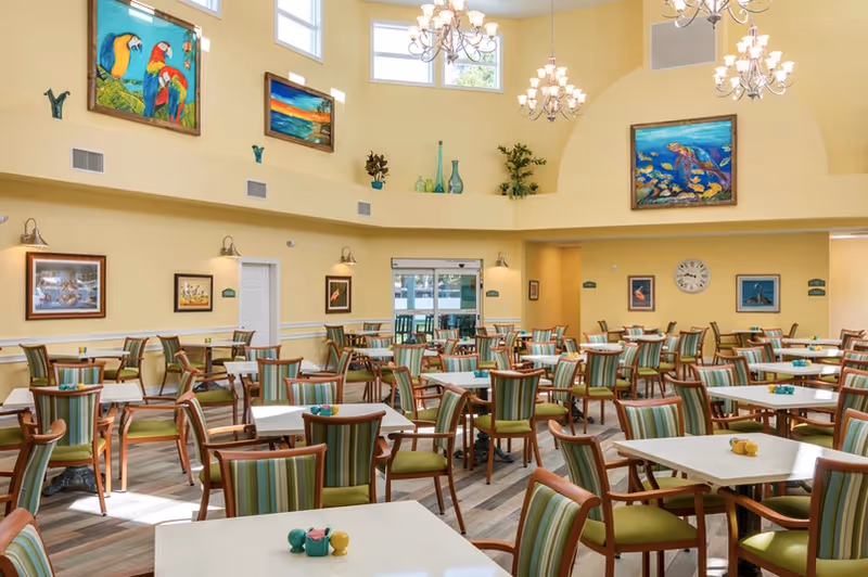 Bright, spacious dining room with multiple tables and striped green chairs, high yellow vaulted ceilings, chandeliers, and colorful wall art.