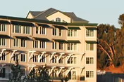 Exterior view of a multi-story residential building with balconies and large windows, surrounded by trees and greenery during daylight.