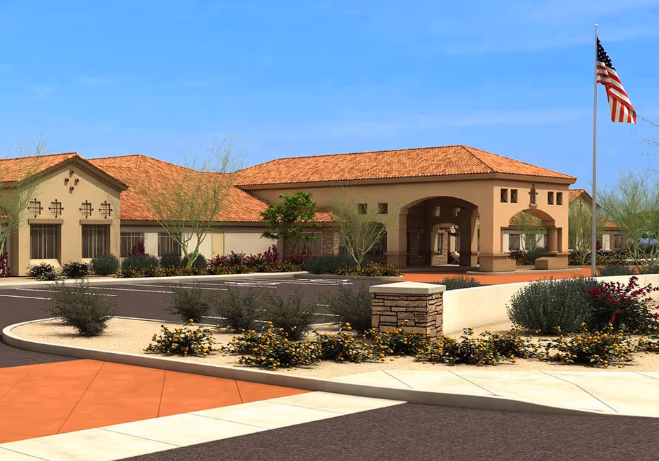 Front exterior of a single-story Mediterranean-style memory care building with a porte-cochère, landscaped circular drive, and an American flag.