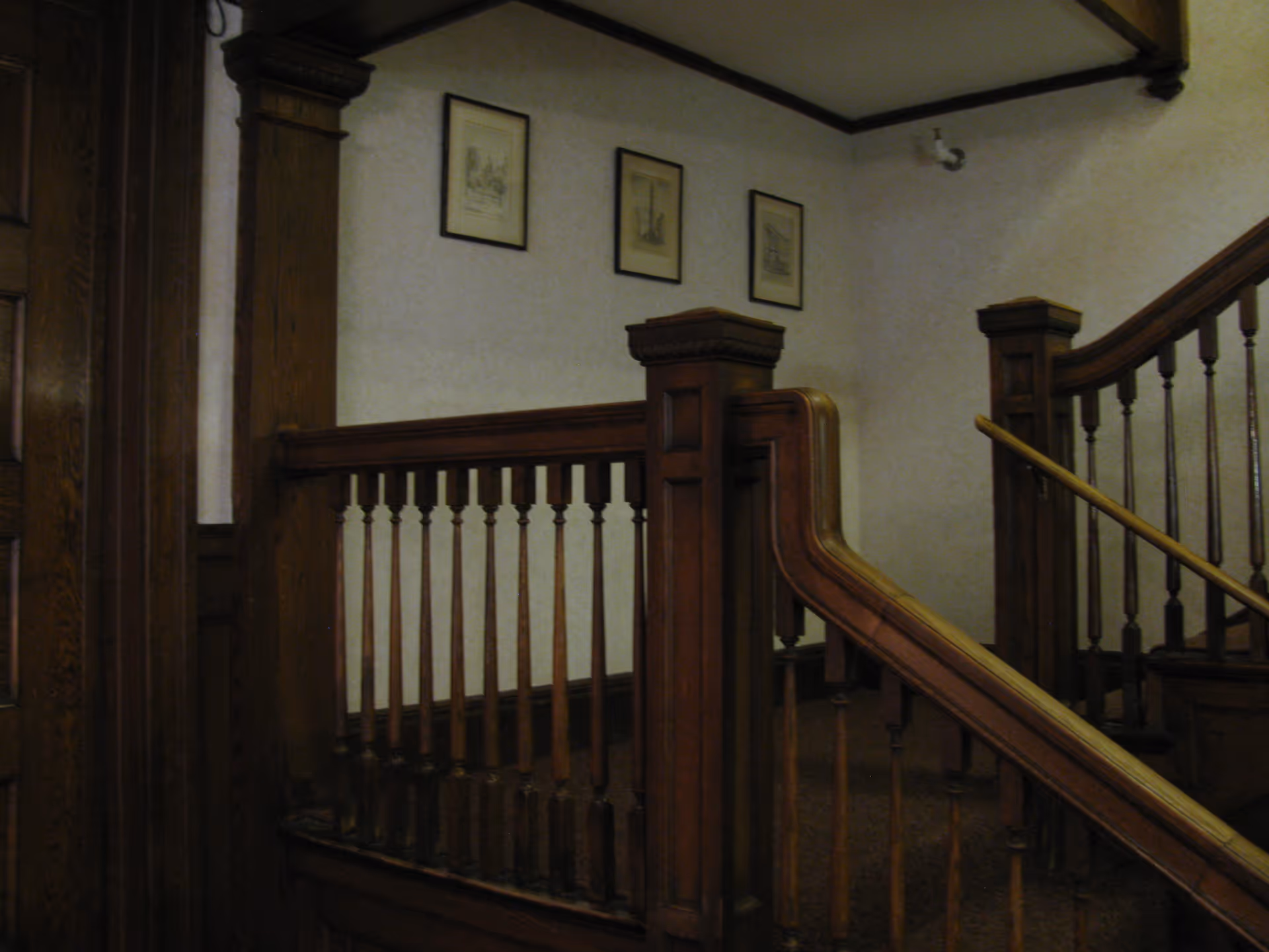 Interior view of a wooden staircase and banister with framed pictures on the wall.