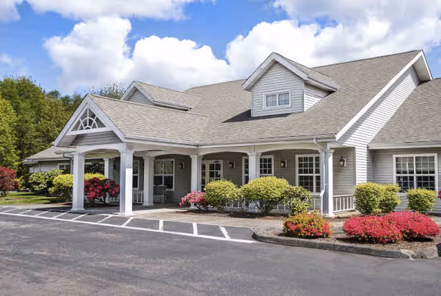 Front exterior of a single-story senior living building with a covered porch, white columns, and landscaped shrubs.