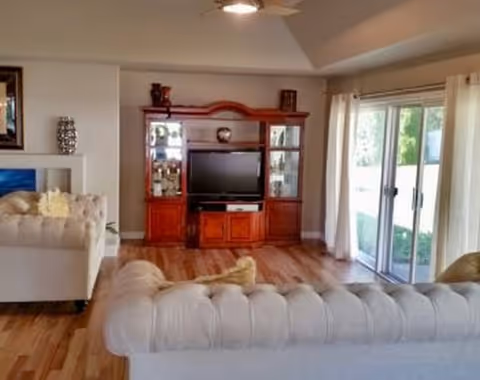 Bright living room with tufted white sofas, a wooden entertainment cabinet, and sliding glass doors.
