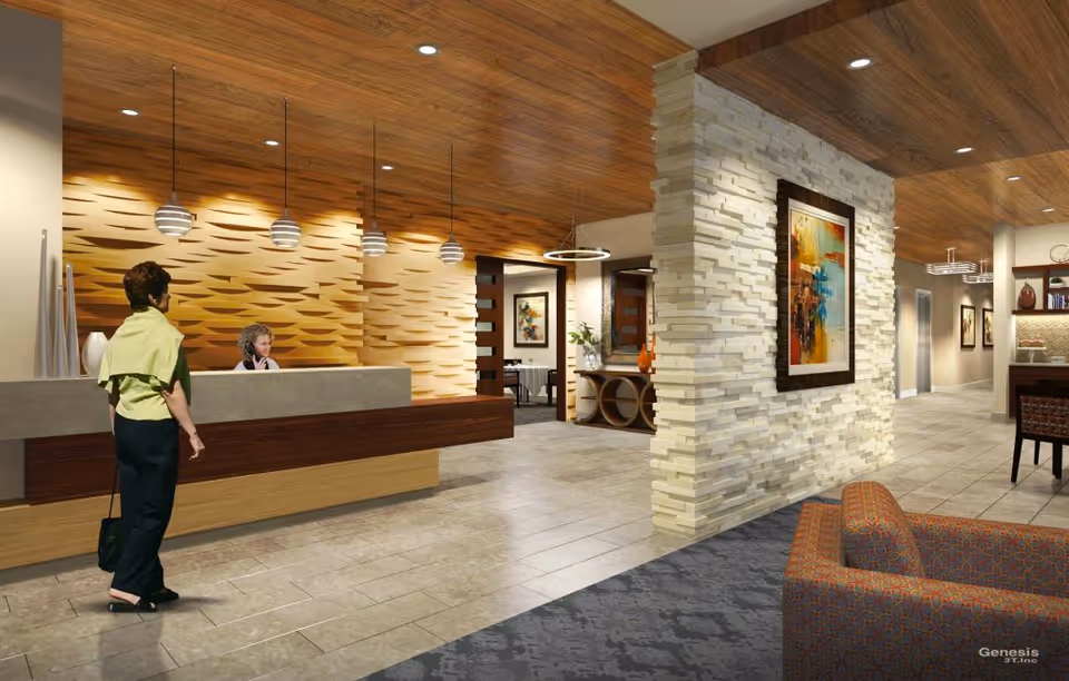 Interior view of a senior living facility reception area with a woman standing at the front desk where a receptionist is seated. The space features modern decor with a textured wooden wall behind the desk, pendant lights, a stone accent wall with a colorful framed painting, and comfortable seating in the foreground.