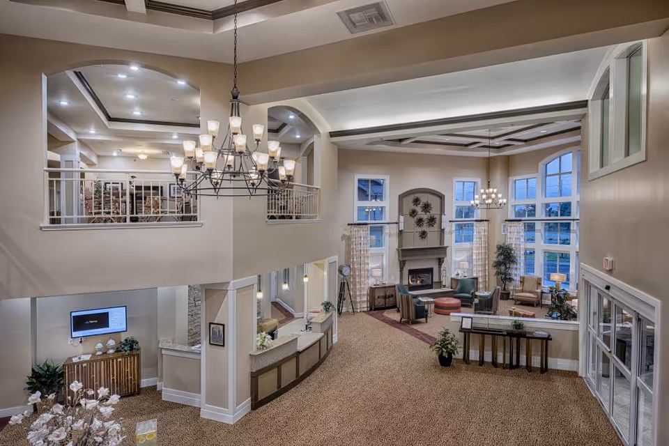 Spacious two-story lobby with a chandelier, reception desk, seating area and fireplace under large windows.