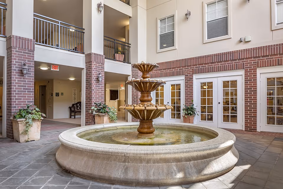 Indoor courtyard featuring a three-tier stone fountain surrounded by potted plants and French doors.