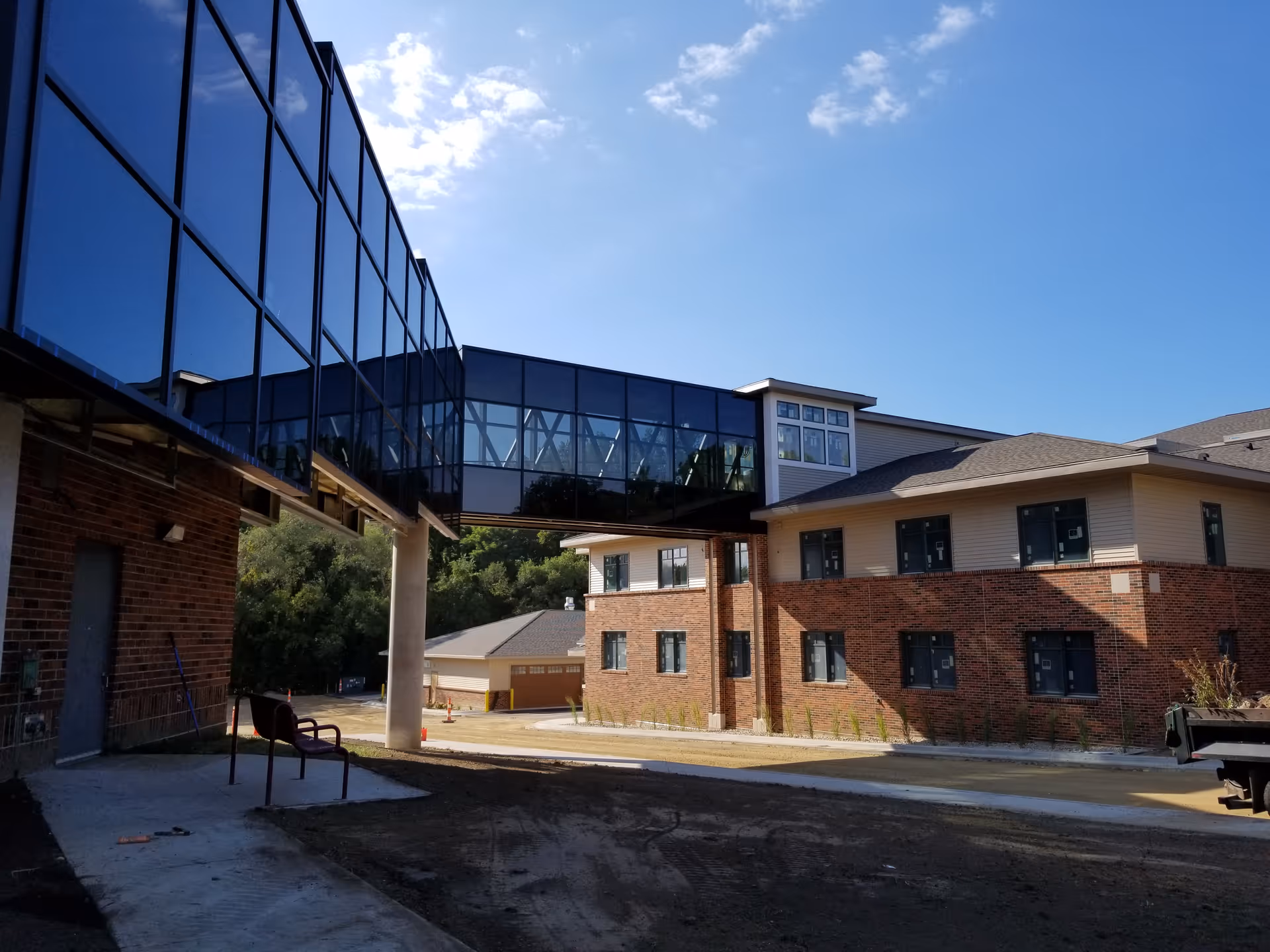 Exterior of a brick multi-story building connected to another structure by a glass-enclosed skybridge under a clear blue sky.