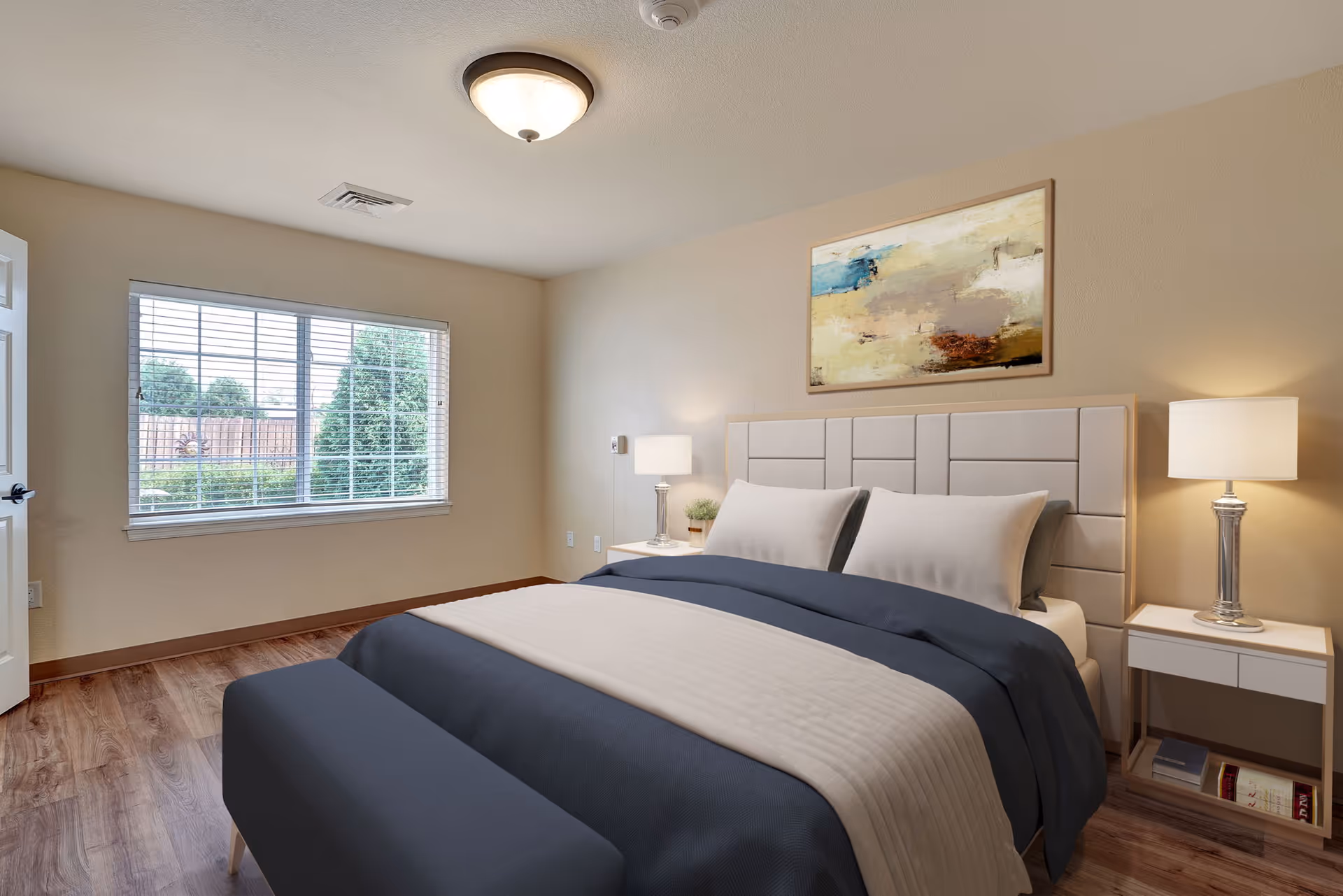 A furnished bedroom with a large bed, nightstands and lamps, a window with blinds, and wall artwork.