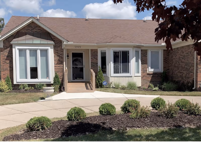 Front view of Harmony Assisted Living Tiverton with brick facade, entry stairs, and landscaped walkway.